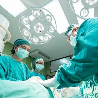 Medicinsko osebje oblečeno v zelene halje in z maskami, operirajo pacienta v operacijski sobi.