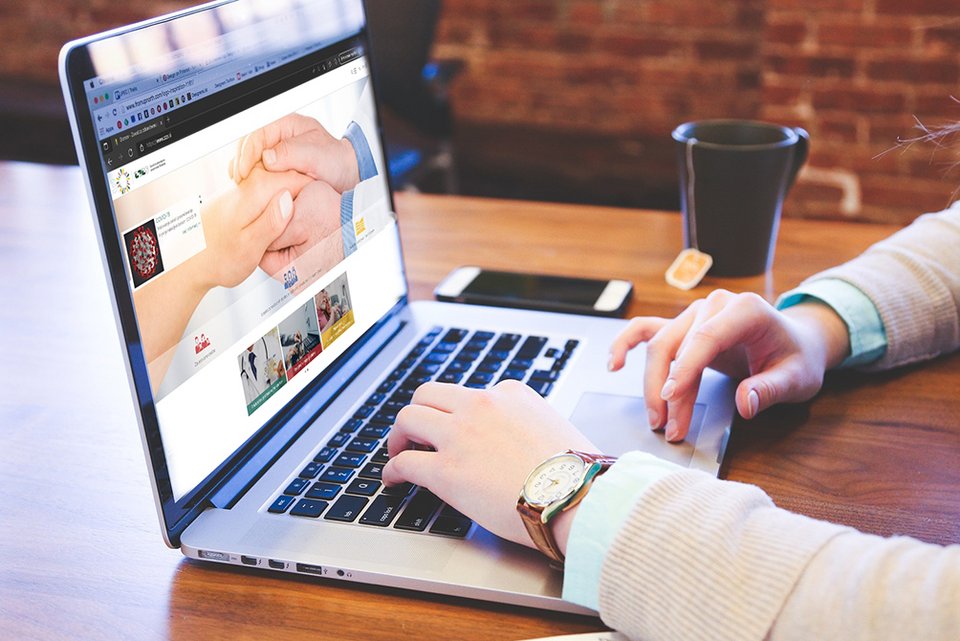 Simbolna slika prenosnika z vidno vstopno stranjo ZZZS, mobitelom, skodelico čaja in rokama, ki se naslanjata na prenosnik